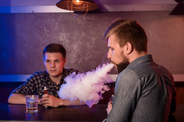 Dos jóvenes fuman cigarrillos electrónicos en un vapebar. tienda de vapeo