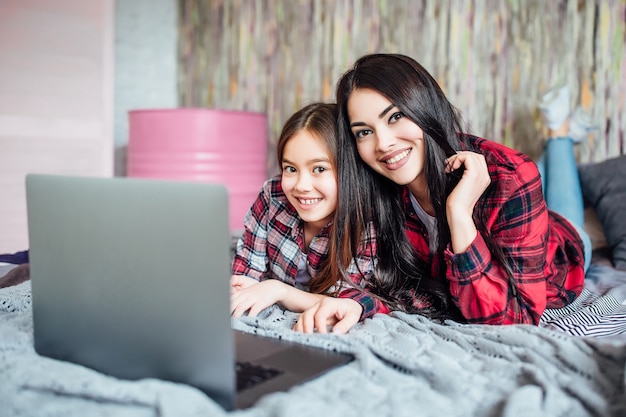 Foto gratuita dos jóvenes hermanas de adolescentes usando un portátil para buscar reuniones de películas en casa en la habitación de la cama