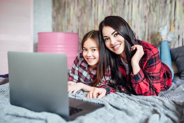 Dos jóvenes hermanas de adolescentes usando un portátil para buscar reuniones de películas en casa en la habitación de la cama