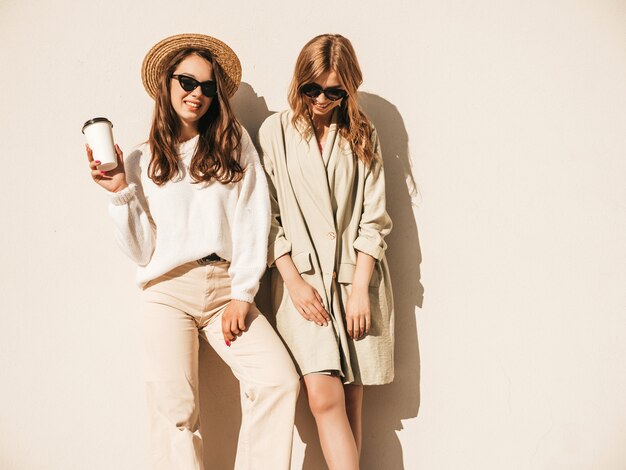 Dos jóvenes hermosas chicas hipster sonrientes en abrigo y suéter blanco de moda