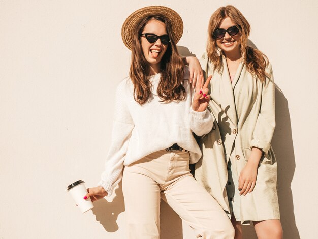 Dos jóvenes hermosas chicas hipster sonrientes en abrigo y suéter blanco de moda