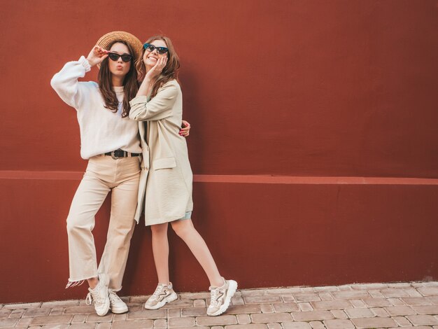 Dos jóvenes hermosas chicas hipster sonrientes en abrigo y suéter blanco de moda