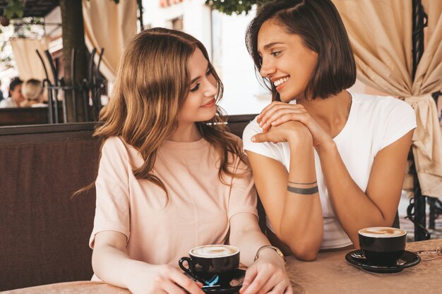 Dos jóvenes hermosas chicas hipster sonrientes en ropa casual de verano de moda. Mujeres despreocupadas charlando en la terraza terraza café y tomando café. Modelos positivos divirtiéndose y comunicándose