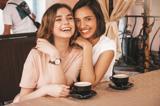 Dos jóvenes hermosas chicas hipster sonrientes en ropa casual de verano de moda. Mujeres despreocupadas charlando en la terraza terraza café y tomando café. Modelos positivos divirtiéndose y comunicándose