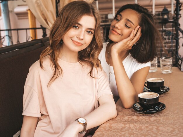 Dos jóvenes hermosas chicas hipster sonrientes en ropa casual de verano de moda. Mujeres despreocupadas charlando en la terraza terraza café y tomando café. Modelos positivos divirtiéndose y comunicándose