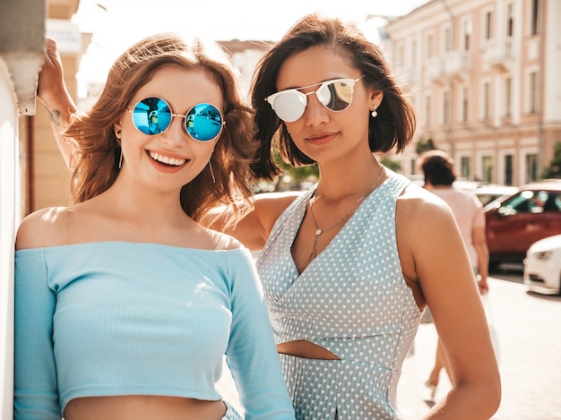 Dos jóvenes hermosas chicas hipster sonrientes en ropa de moda de verano. Mujeres despreocupadas sexy posando en el fondo de la calle en gafas de sol. Modelos positivos divirtiéndose y abrazándose