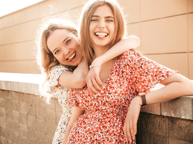 Dos jóvenes hermosas chicas hipster sonrientes en vestido de verano de moda. Mujeres despreocupadas sexy posando en el fondo de la calle. Modelos positivos divirtiéndose y mostrando lenguas