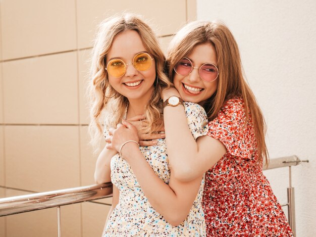 Dos jóvenes hermosas chicas hipster sonrientes en vestido de verano de moda. Mujeres despreocupadas sexy posando en el fondo de la calle con sombreros. Modelos positivos divirtiéndose y abrazándose. Se están volviendo locos