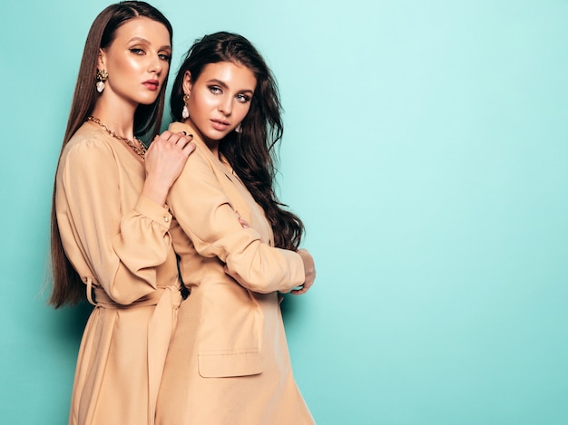 Dos jóvenes hermosas chicas morenas en ropa de verano agradable. Mujeres despreocupadas sexy posando junto a la pared azul en el estudio