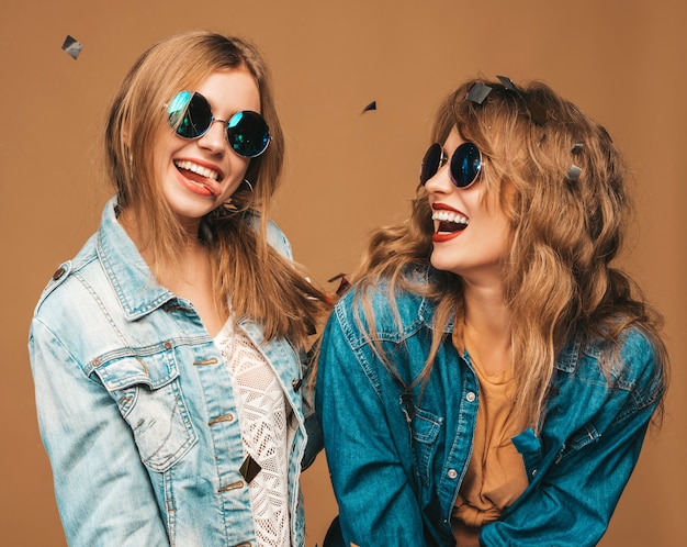 Dos jóvenes hermosas chicas sonrientes en ropa de verano de moda y gafas de sol. Sexy mujer despreocupada posando. Modelos de gritos positivos bajo confeti