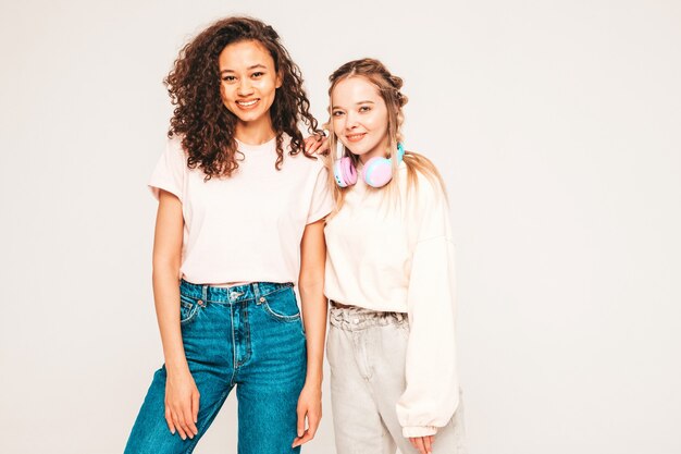 Dos jóvenes hermosas mujeres hipster internacional sonriente en ropa de moda de verano. mujeres despreocupadas, posar, en, estudio