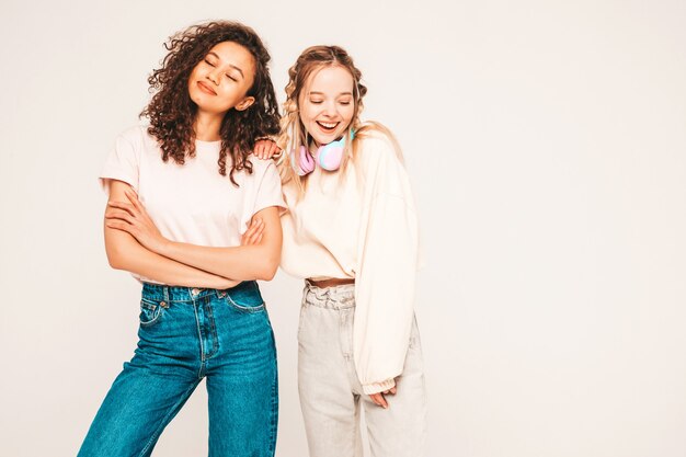 Dos jóvenes hermosas mujeres hipster internacional sonriente en ropa de moda de verano. mujeres despreocupadas, posar, en, estudio