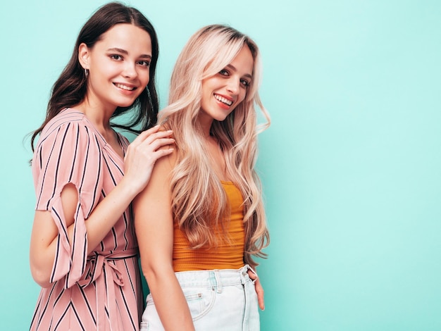 Dos jóvenes hermosas mujeres hipster morena sonriente en ropa de verano de moda Mujeres sexy despreocupadas posando junto a la pared azul Modelos positivos divirtiéndose Alegre y feliz
