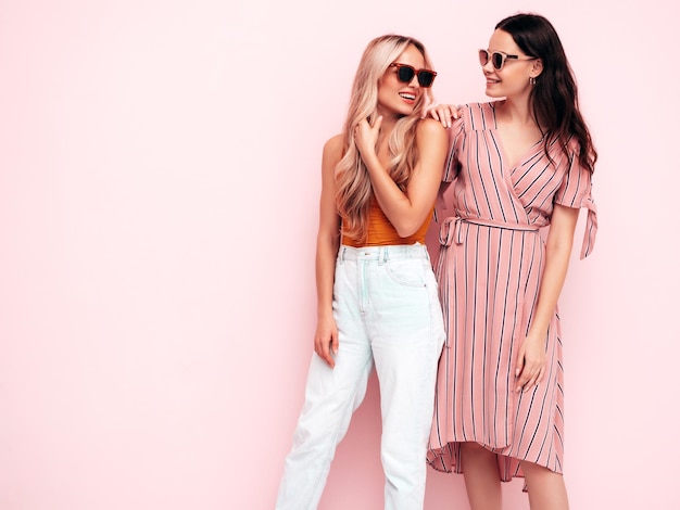 Dos jóvenes hermosas mujeres hipster morena sonriente en ropa de verano de moda Mujeres sexy despreocupadas posando junto a la pared rosa Modelos positivos divirtiéndose Alegre y feliz En gafas de sol