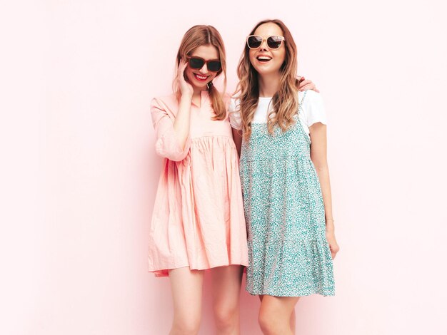Dos jóvenes hermosas mujeres hipster morena sonriente en vestidos de verano de moda Mujeres sexy despreocupadas posando junto a la pared rosa Modelos positivos divirtiéndose Alegre y feliz