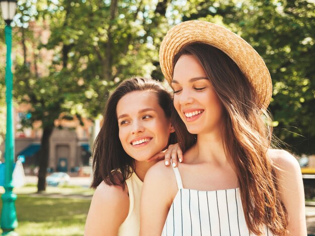 Dos jóvenes hermosas mujeres hipster sonrientes con ropa de verano de moda. Mujeres sexy y despreocupadas posando en el fondo de la calle con sombrero Modelos puros positivos divirtiéndose al atardecer abrazándose y volviéndose locos