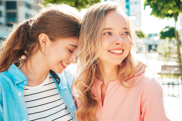 Dos jóvenes hermosas mujeres hipster sonrientes con ropa de verano de moda y vestido. Mujeres sexys y despreocupadas posando en el fondo de la calle Modelos puros positivos divirtiéndose al atardecer abrazándose y volviéndose locos