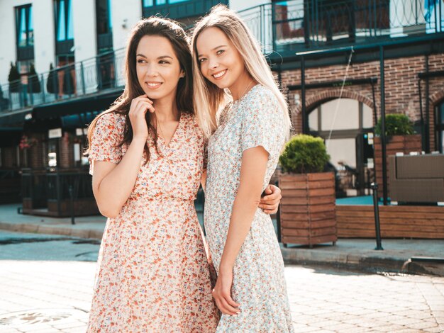 Dos jóvenes hermosas mujeres hipster sonrientes en vestidos de verano de moda Mujeres sexy despreocupadas posando en la calle Modelos puros positivos divirtiéndose al atardecer abrazándose y volviéndose locos