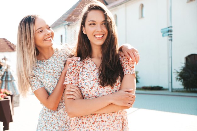 Dos jóvenes hermosas mujeres hipster sonrientes con vestidos de verano de moda. Mujeres sexys y despreocupadas posando en la calle. Modelos puros positivos divirtiéndose al atardecer abrazándose y volviéndose locos. Feliz y alegre.