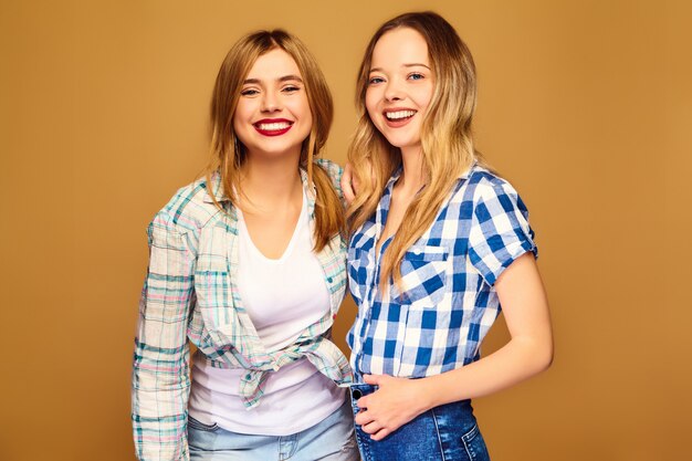 Dos jóvenes hermosas rubias sonrientes en camisas a cuadros de verano de moda