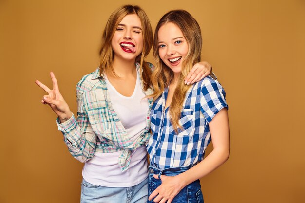 Dos jóvenes hermosas rubias sonrientes en camisas a cuadros de verano de moda