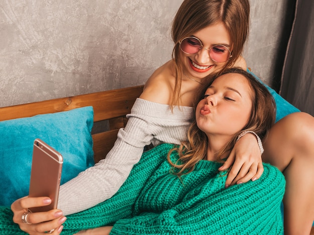 Dos jóvenes hermosas sonrientes hermosas chicas en ropa de moda de verano. Mujeres despreocupadas sexy posando en el interior y tomando selfie. Modelos positivos divirtiéndose con el teléfono inteligente.