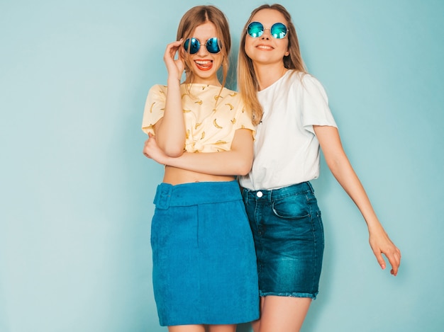 Dos jóvenes hermosas sonrientes rubias hipster chicas en jeans moda verano faldas ropa.