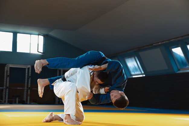 Dos jóvenes luchadores de judo en kimono entrenando artes marciales en el gimnasio con expresión en acción y movimiento