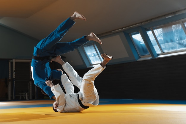 Dos jóvenes luchadores en kimono entrenando artes marciales en el gimnasio