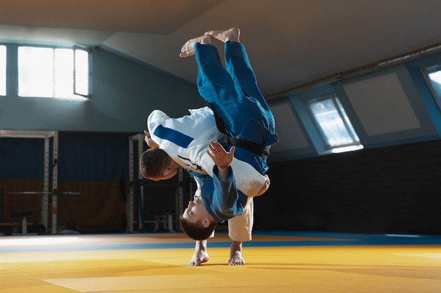 Dos jóvenes luchadores en kimono entrenando artes marciales en el gimnasio
