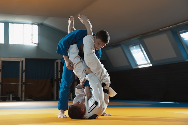 Dos jóvenes luchadores en kimono entrenando artes marciales en el gimnasio