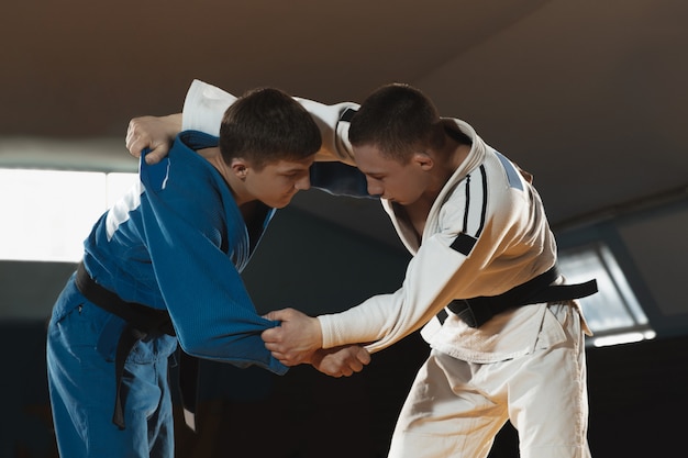 Foto gratuita dos jóvenes luchadores en kimono entrenando artes marciales en el gimnasio