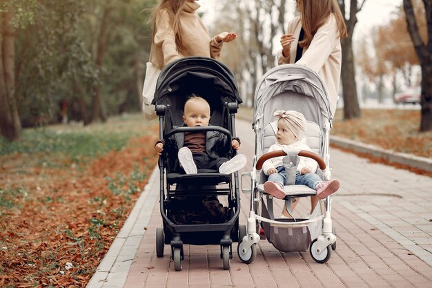 Dos jóvenes madres caminando en un parque de otoño con carruajes