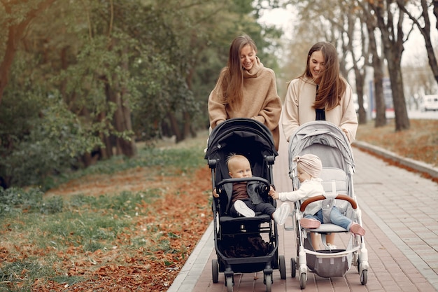 Dos jóvenes madres caminando en un parque de otoño con carruajes