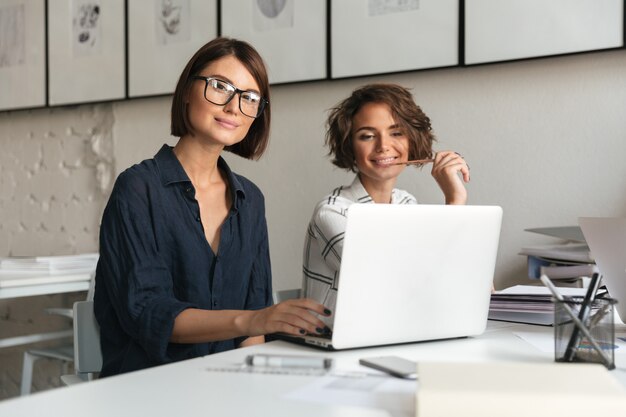 Dos jóvenes mujeres felices trabajando junto a la mesa