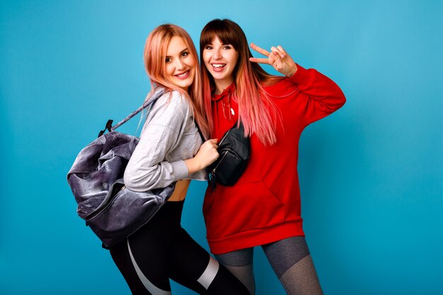 Dos jóvenes mujeres graciosas bastante hipster vistiendo trajes casuales brillantes deportivos, posando sonriendo listo para CrossFit y fitness