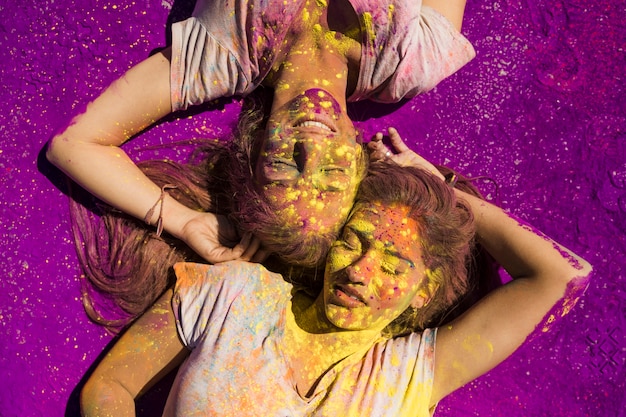 Foto gratuita dos jóvenes mujeres tumbadas sobre polvos de color púrpura del festival holi