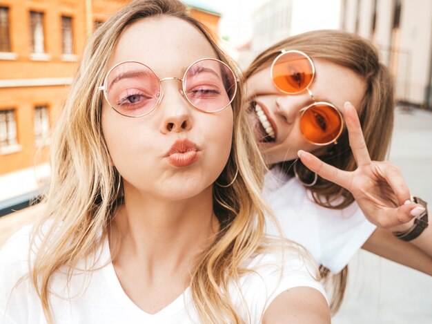 Dos jóvenes sonrientes mujeres rubias hipster en ropa de verano. Chicas tomando fotos de autorretrato autofoto en el teléfono inteligente. .