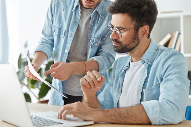 Foto gratuita dos jóvenes trabajadores exitosos colaboran juntos en el espacio de coworking