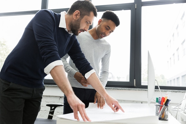 Dos jóvenes trabajadores de oficina masculinos apuntando en un gráfico