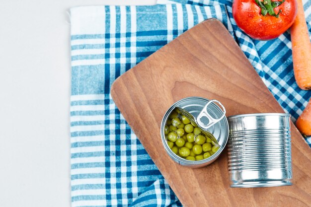 Dos latas de guisantes hervidos, verduras y mantel.