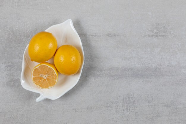 Dos limones enteros y medio en el plato sobre la superficie de mármol