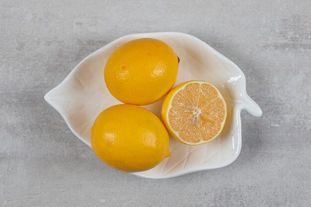 Dos limones enteros y medio en el plato sobre la superficie de mármol