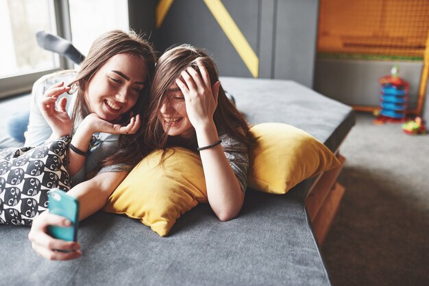 Dos lindas hermanas gemelas sonrientes sosteniendo smartphone y haciendo selfie.