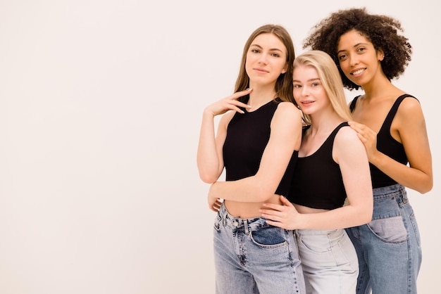 Dos lindas jóvenes caucásicas y afro posando alegremente juntas sobre fondo blanco con espacio para texto Estilo de vida étnico diverso