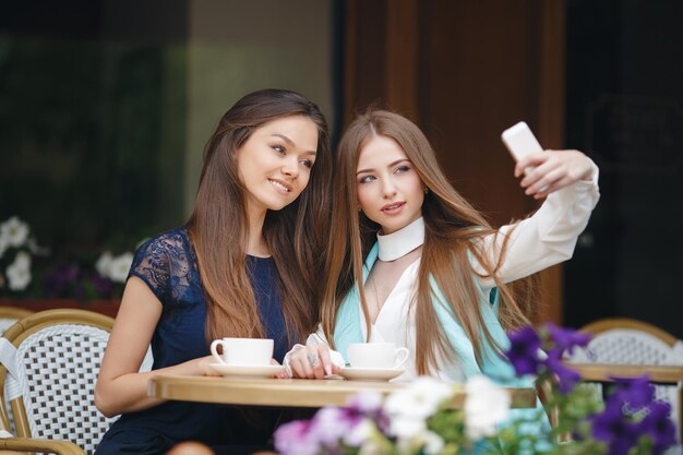 dos lindas mujeres jóvenes en un café con café y teléfono