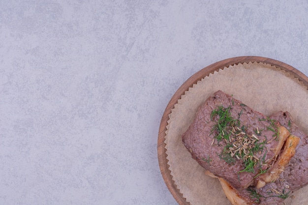 Dos lonchas de bistec con hierbas y especias en un plato de madera.