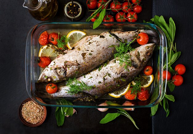 Dos lubina al horno en una fuente para horno con especias en una mesa negra. Vista superior