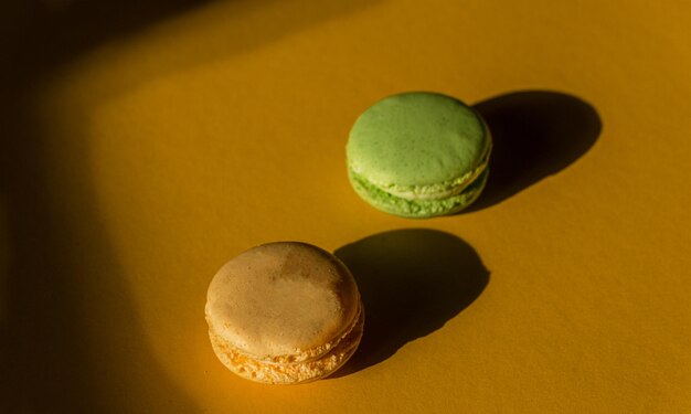 Dos macarons aislados amarillos y verdes sobre un suelo amarillo que muestran sus sombras