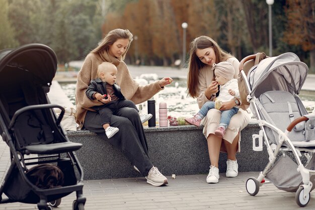 Dos madres jóvenes sentadas en un parque de otoño con carruajes